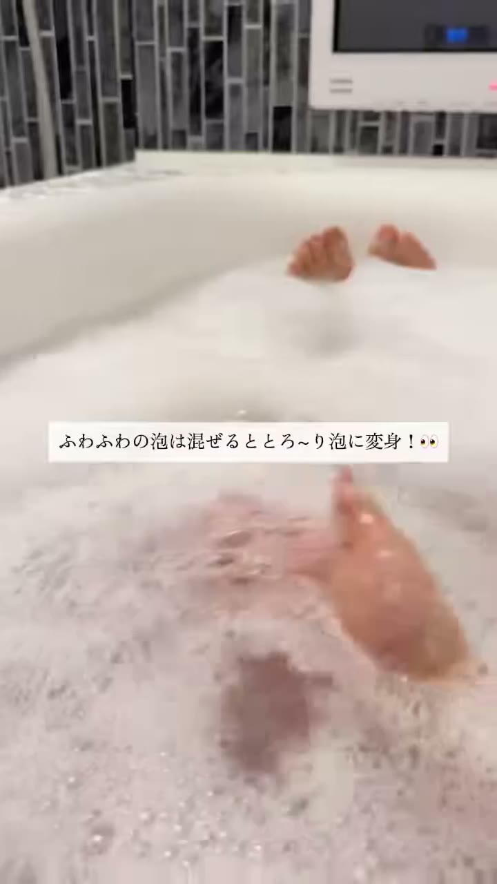 泡でいっぱいの浴槽で、手で泡をお湯に混ぜている様子