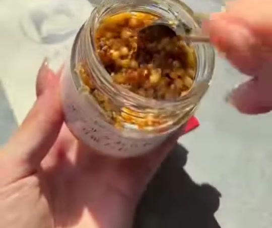 ふたを開けたびんの中の、油がからんだあられなどの粒をスプーンですくっている様子
