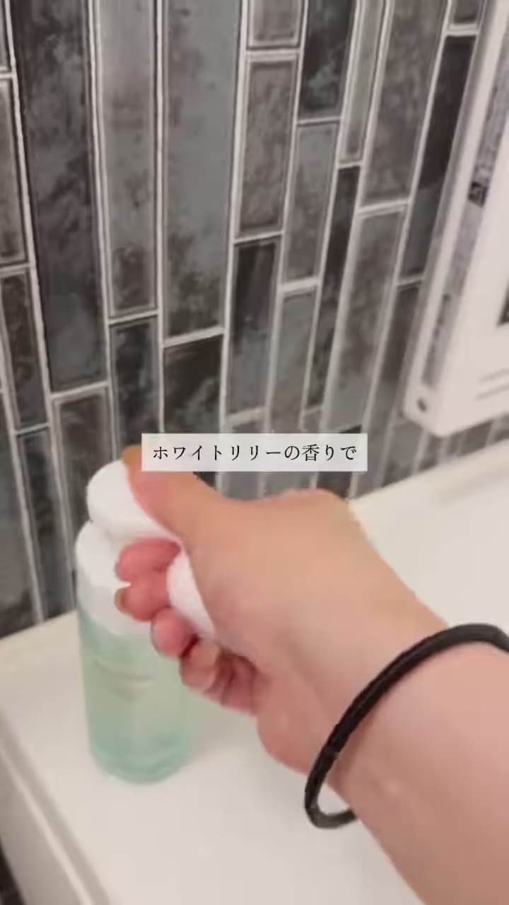 グレーのタイル壁の浴室で、浴槽のふちに置いたボトルのポンプを手で押している場面