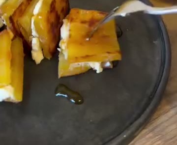 黒い皿の上の、焼き目のついた干し芋に白いクリーム状のものをはさんで切り分けたものを、フォークで取っている様子