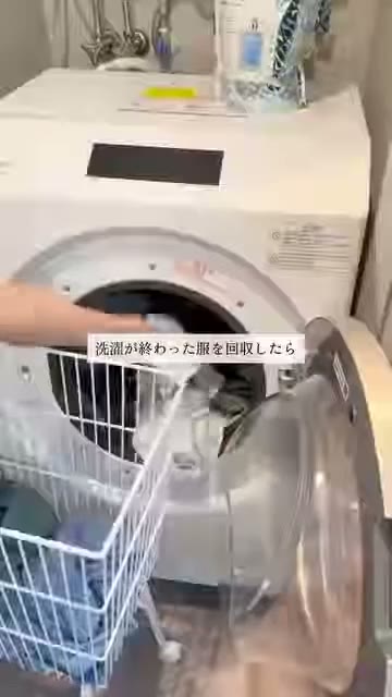 洗濯機の前に置いたワイヤーのかごに、洗濯機から取り出した服を入れている様子